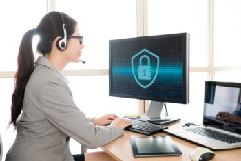 professional pretty female office worker wearing headset talking with customer and typing data into online system to solve cyber security problem.