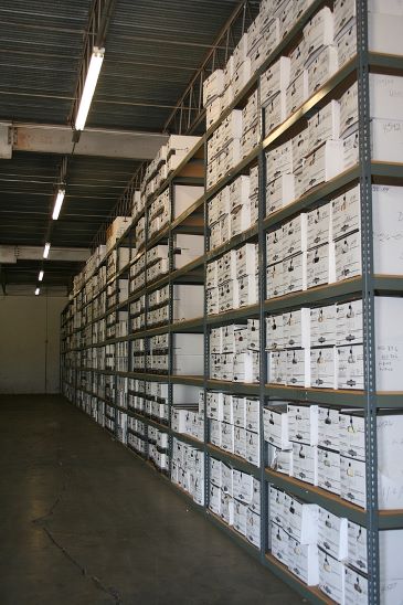 Hundreds of white archive boxes are shown stored on racks at a records storage warehouse facility.