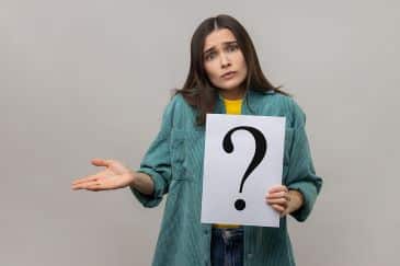 Portrait of confused puzzled woman looking at camera, holding paper with question mark.