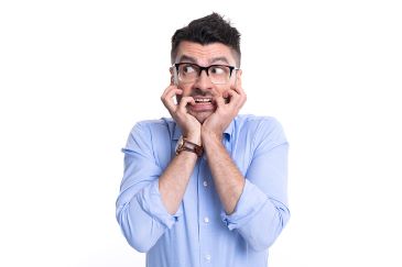 A man in a dress shirt is biting his nails and looking sideways in fear.