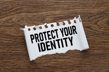 The words "Protect Your Identity" are shown in black letters on a white piece of torn paper that is laying on a table surface.