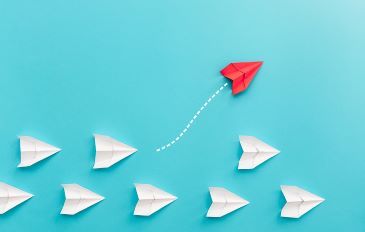 A group of white paper airplanes on a light blue background with one red plane flying off in another direction