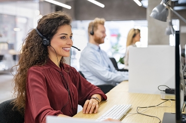 Call center worker talking on the phone with a headset with colleagues behind her in soft focus.