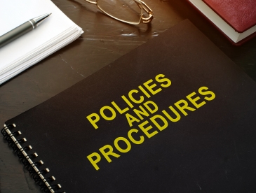 Black coil-bound notebook with gold letters reading, "Policies and Procedures"