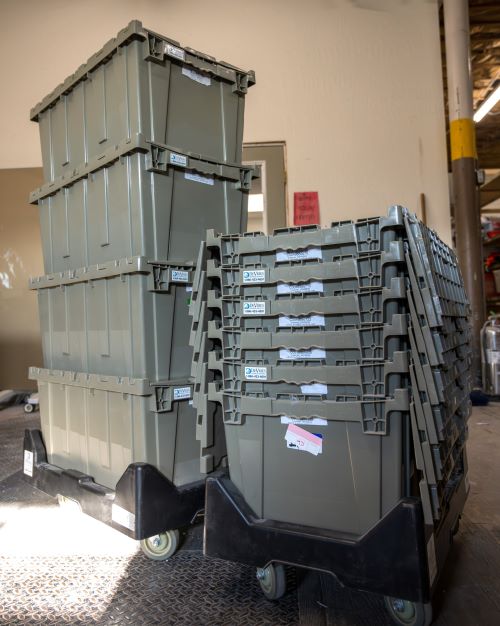 Grey plastic totes are stacked on dolly carts.
