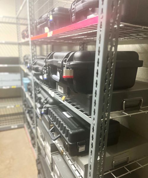 Secure, locked, black storage cases are shown on industrial shelving in a dedicated storage room.