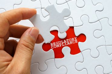 Hand holding a white puzzle piece, ready to place in last spot, labeled REGULATORY COMPLIANCE