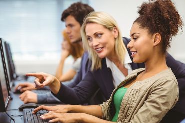 A teacher is talking to her student in computer class at a university.