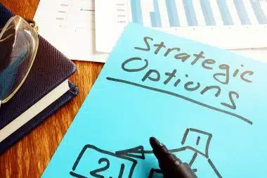A blue paper with the handwritten words Strategic Options sits on a desk surface.