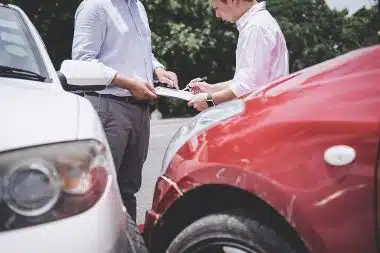 Insurance Agent and client are examining a damaged car and customer is signing report at crash scene.