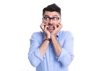 A man in a dress shirt is biting his nails and looking sideways in fear.