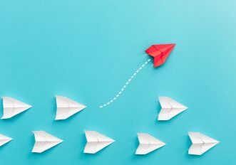 A group of white paper airplanes on a light blue background with one red plane flying off in another direction