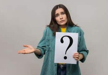 Portrait of confused puzzled woman looking at camera, holding paper with question mark.