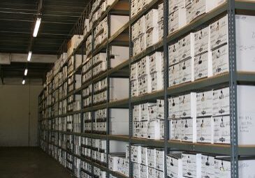 Hundreds of white archive boxes are shown stored on racks at a records storage warehouse facility.