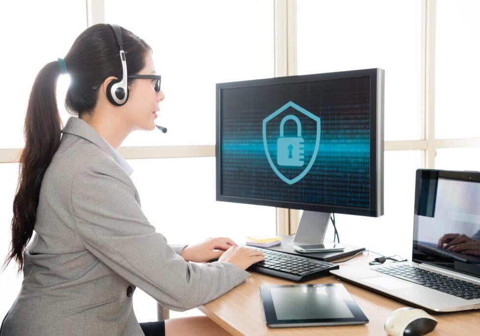 professional pretty female office worker wearing headset talking with customer and typing data into online system to solve cyber security problem.