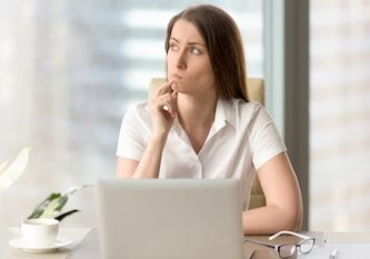 Woman with pensive facial expression looking aside while sitting at workplace. Unsure businesswoman thinking about difficult question. Female office worker doubted because of uncertain situation