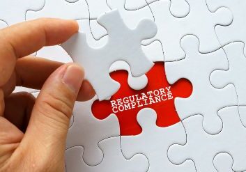 Hand holding a white puzzle piece, ready to place in last spot, labeled REGULATORY COMPLIANCE
