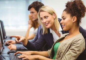 A teacher is talking to her student in computer class at a university.