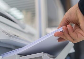 Closeup image of a person's hand feeding a stack of paper into a printer/scanner