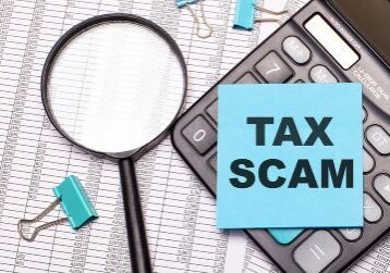 On the table are reports, a magnifying glass, a calculator, and a blue note sticker with the word TAX SCAM.