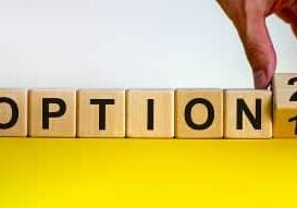 A series of side by side wood cubes spell out the word OPTION and a hand reaches in to flip the final cube from the number 1 to number 2.