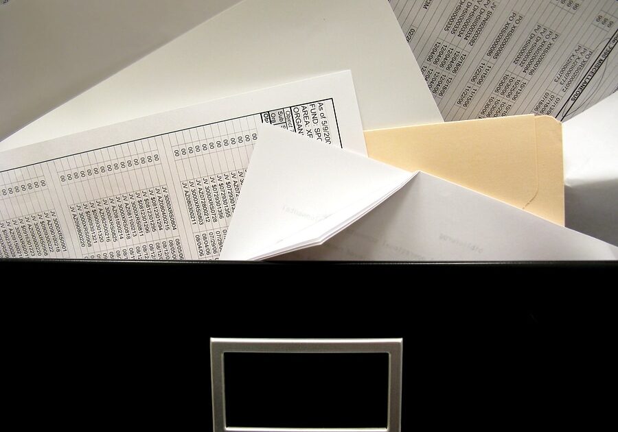 Overflowing messy office filing cabinet drawer spills spreadsheets and other documents.