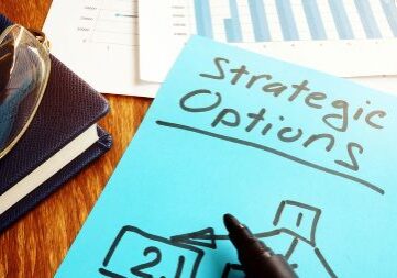 A blue paper with the handwritten words Strategic Options sits on a desk surface.